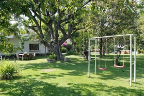 Un jardín con un columpio, una zona de comedor y un gran árbol.