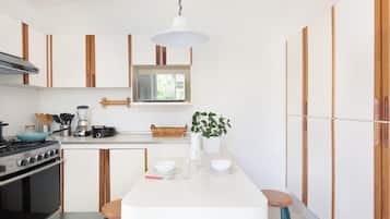 A modern kitchen with wooden cabinets, a stove, a dining table with stools, and a hanging light fixture.