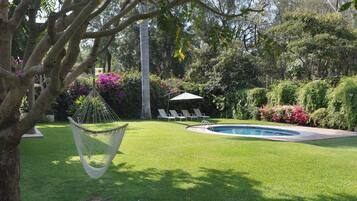 Patio trasero con piscina, una hamaca y una zona de estar con sombrillas.