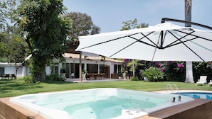 Una piscina con hidromasaje, rodeada por una terraza con mobiliario exterior y una gran sombrilla que proporciona sombra.