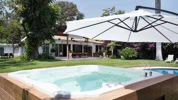 Una piscina con hidromasaje, rodeada por una terraza con mobiliario exterior y una gran sombrilla que proporciona sombra.