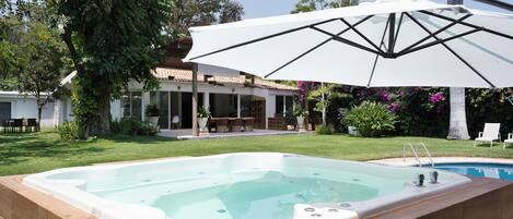 A swimming pool with a hot tub, surrounded by a patio area with outdoor furniture and a large umbrella providing shade.