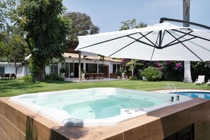 Una piscina con hidromasaje, rodeada por una terraza con mobiliario exterior y una gran sombrilla que proporciona sombra.