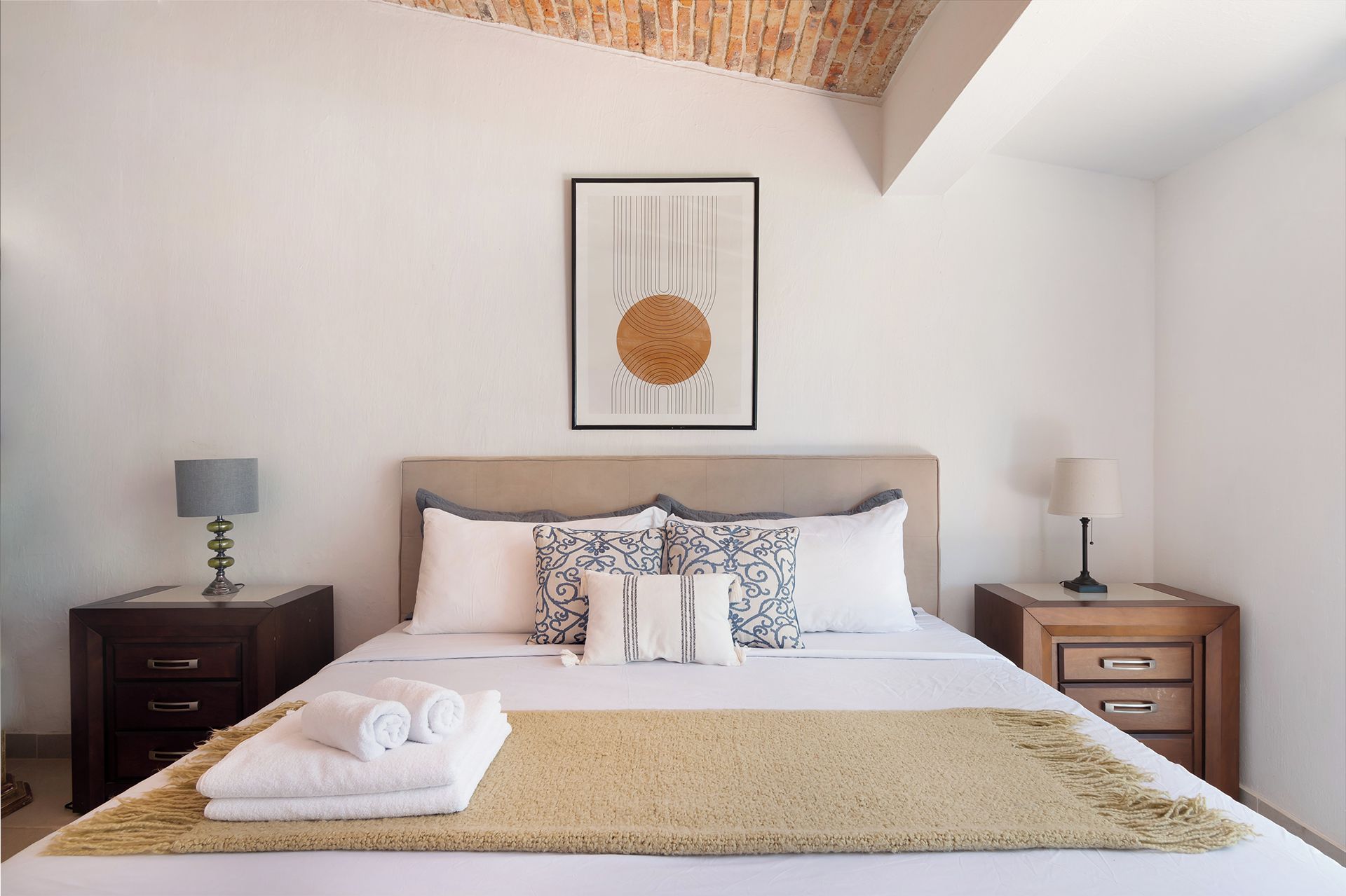 A neatly made bed with a beige rug, two bedside tables with lamps, and a framed artwork above the bed.
