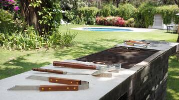 Una parrilla con diversos utensilios y una piscina al fondo.