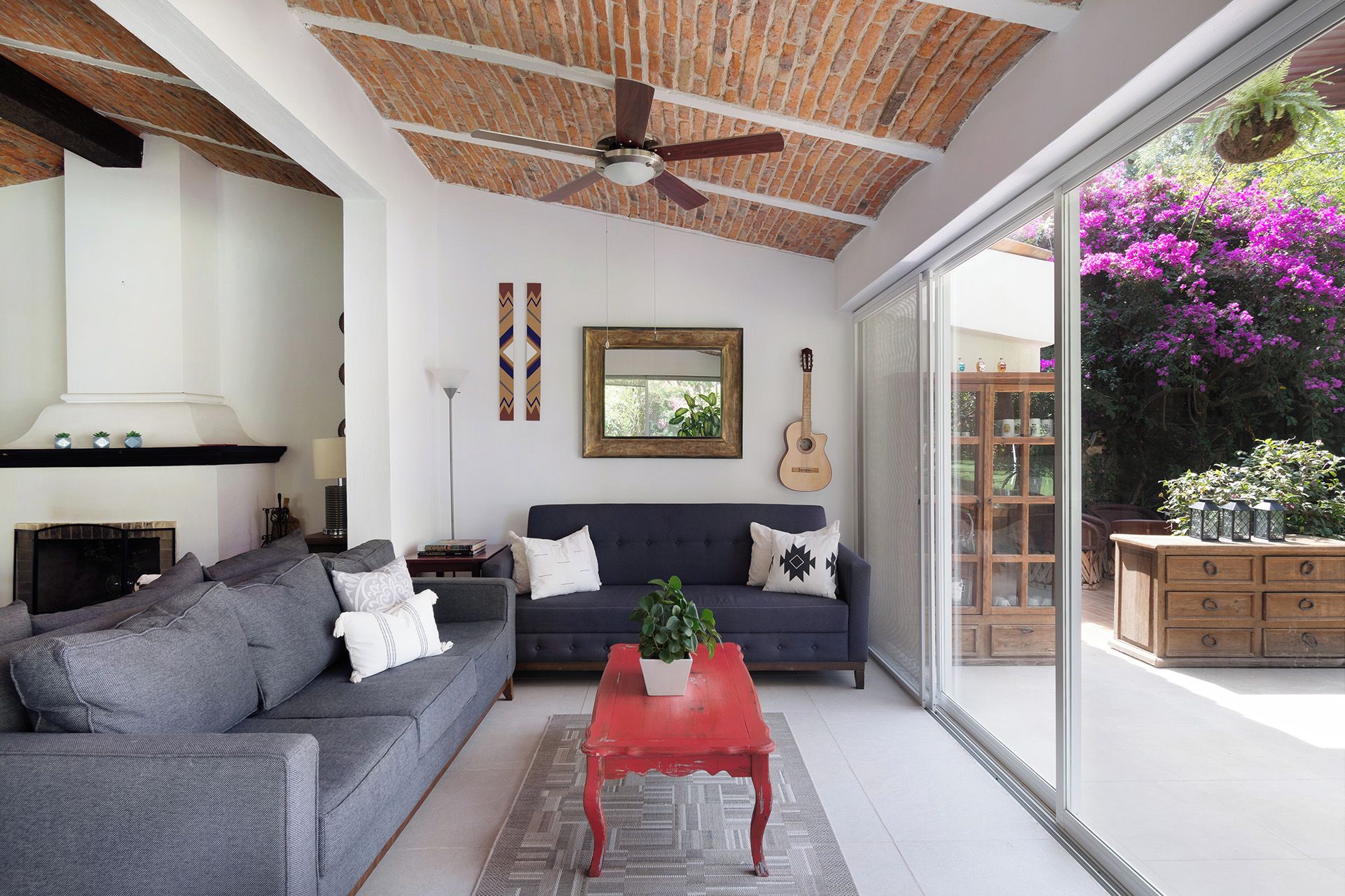 A living room with a fireplace, a sofa, a red coffee table, and a guitar on the wall.