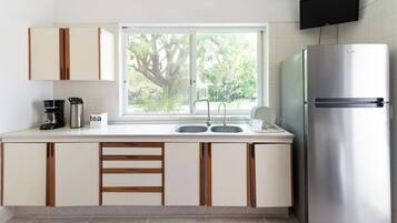 A modern kitchen with a stainless steel refrigerator, double sink, and a window with a view of greenery.