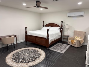 A bedroom with a four-poster bed, a desk, a chair, a standing lamp, and an air conditioning unit. - Cozy 1-bedroom studio in soothing Fredericksburg (Fredericksburg)