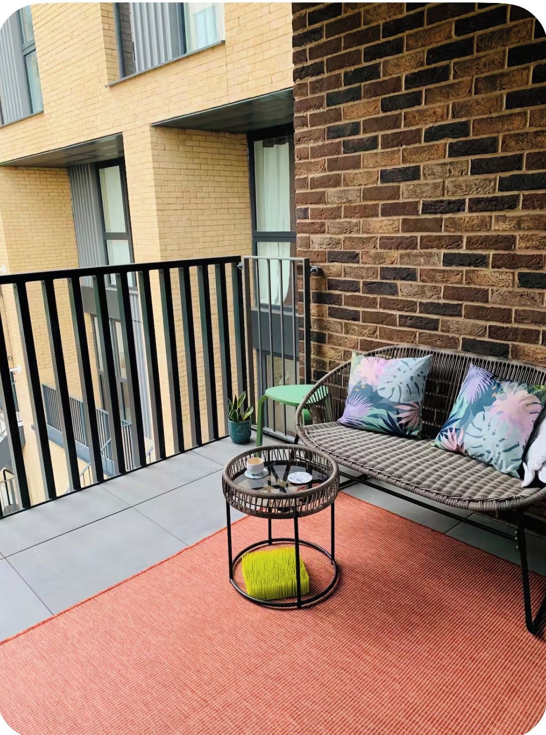 Een balkon met een rieten bank, een klein rond tafeltje met een kopje en een potplant.