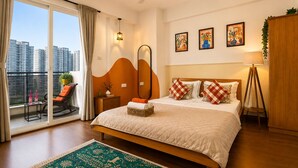Una camera d'albergo con un letto grande, un balcone con una sedia, una ventola a soffitto e opere d'arte alle pareti.