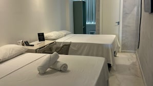 Ett hotellrum med två sängar, ett skrivbord med en telefon och en skylt, samt ett fönster med persienner.