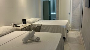 A hotel room with two beds, a desk with a phone and a sign, and a window with blinds. - Hotel Novo Centro (Petrolina)