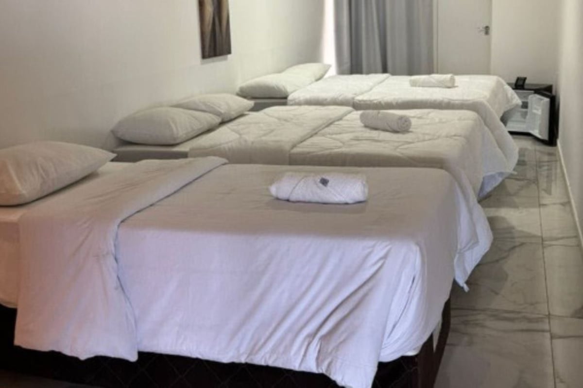 A hotel room with three beds, each with white bedding and pillows.