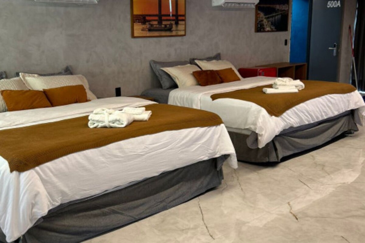 A hotel room with two beds, each with a white and brown bedspread, and a blue door in the background.