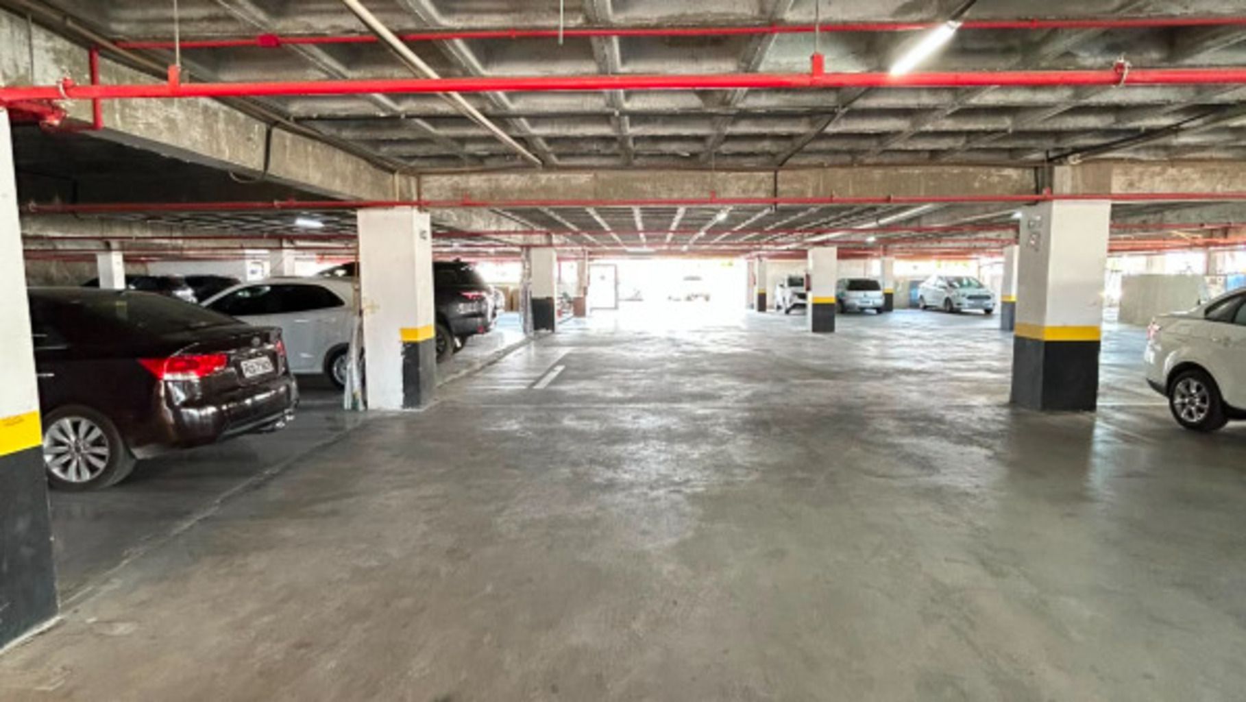 Garagem de estacionamento em vários níveis, com piso de concreto e vigas estruturais vermelhas.