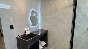 A modern bathroom with a marble wall, a sink with a towel, and a glass shower enclosure.