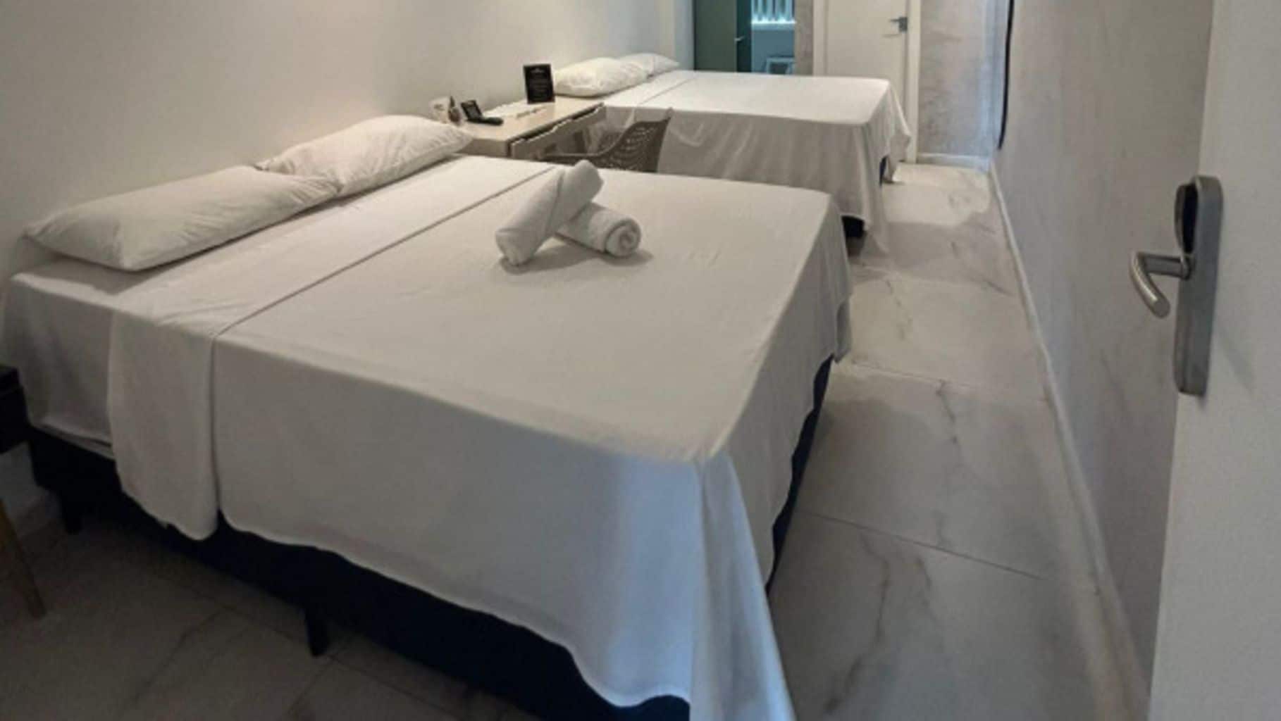 A hotel room with two beds, a nightstand, and a door.
