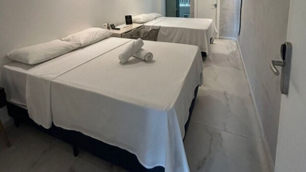 A hotel room with two beds, a nightstand, and a door.