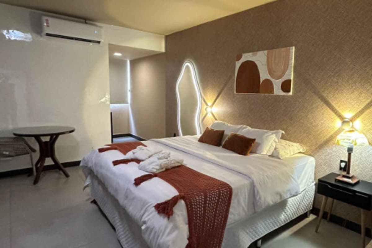 A hotel room with a bed, bedside table, and a wall-mounted light fixture.