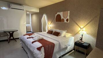 Quarto de hotel com cama, mesa de cabeceira e luminária fixada na parede.