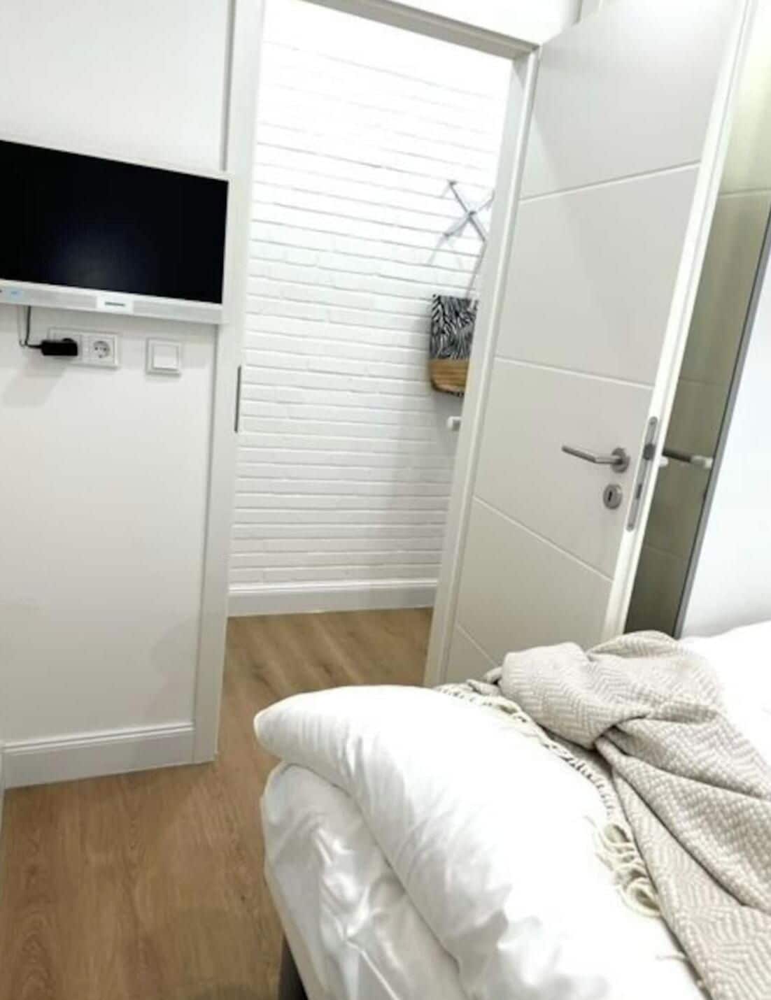 A bedroom with a bed, a wardrobe, a television, and a door leading to a bathroom.