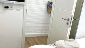 A bedroom with a bed, a wardrobe, a television, and a door leading to a bathroom.