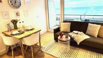 A living room with a dining area, a sofa, a coffee table, and a view of the sea.