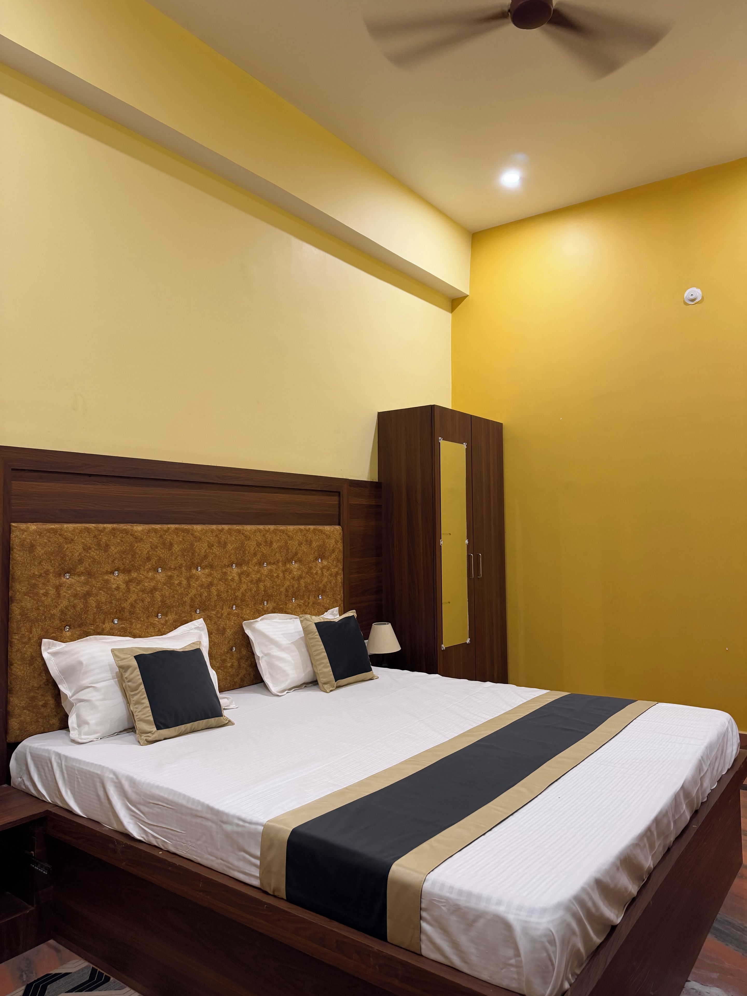 A neatly made bed with a headboard, a bedside lamp, and a wardrobe in a room with yellow walls.