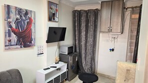 A room with a flat-screen TV, a small refrigerator, a desk with a computer, a chair, and a painting on the wall. - Kamakis,Ruiru (Ruiru)
