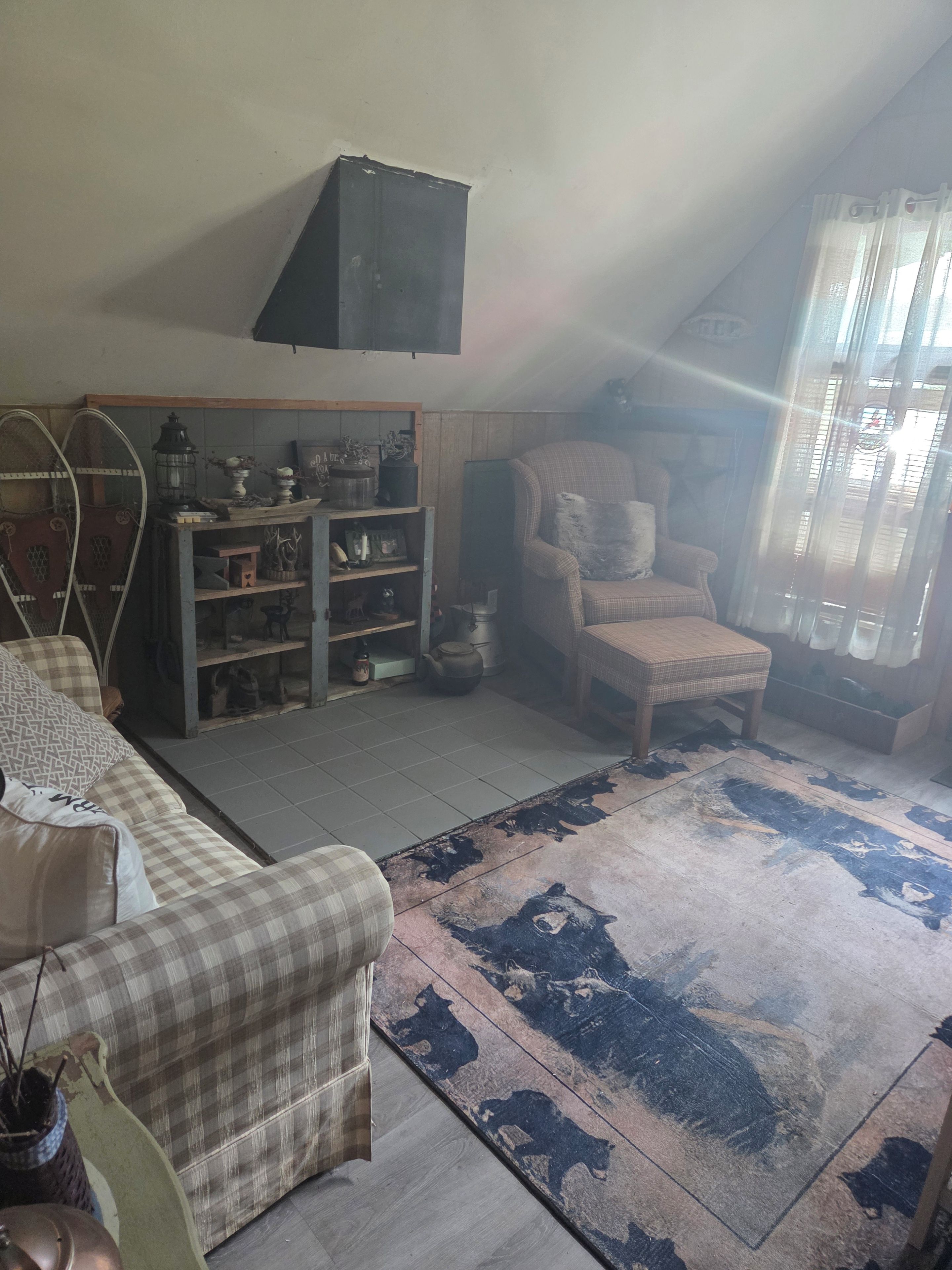 Une pièce chaleureuse avec un canapé à carreaux, un meuble en bois orné d’objets décoratifs, un fauteuil et un tapis à motifs.