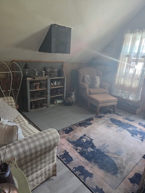 Une pièce chaleureuse avec un canapé à carreaux, un meuble en bois orné d’objets décoratifs, un fauteuil et un tapis à motifs.