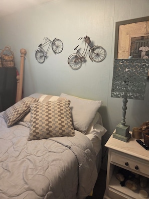A bedroom with a bed, pillows, a nightstand, a lamp, and wall decorations including two bicycles.