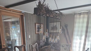 Uma área de jantar com uma longa mesa de madeira, cadeiras, um centro de mesa tecido e luminárias pendentes.
