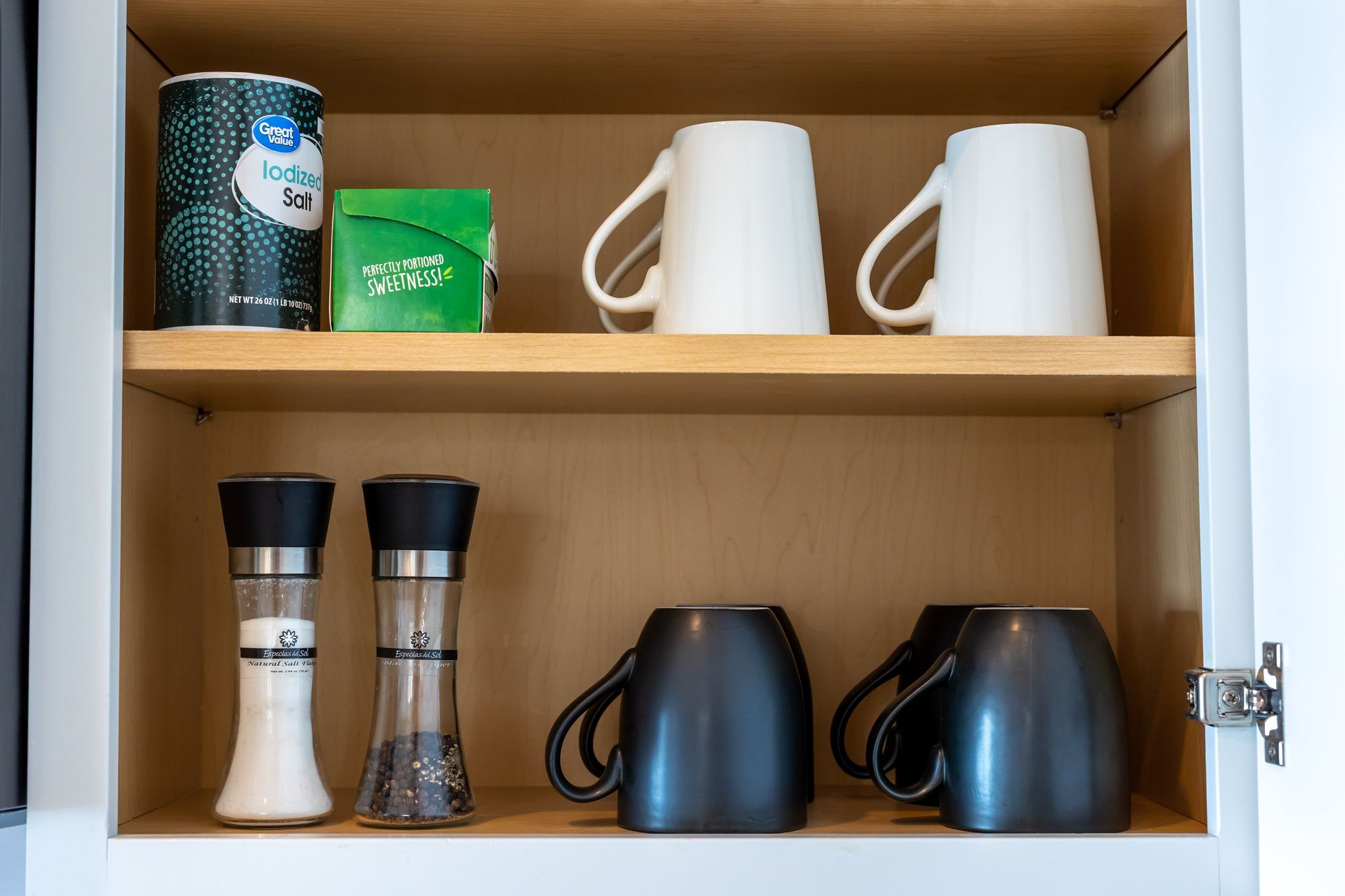 A kitchen cabinet with salt containers, a coffee maker, and two mugs.