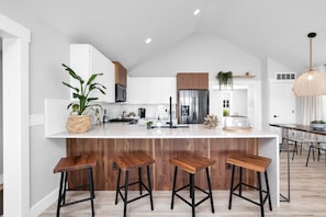 A modern kitchen with white cabinets, a stainless steel refrigerator, and wooden stools.