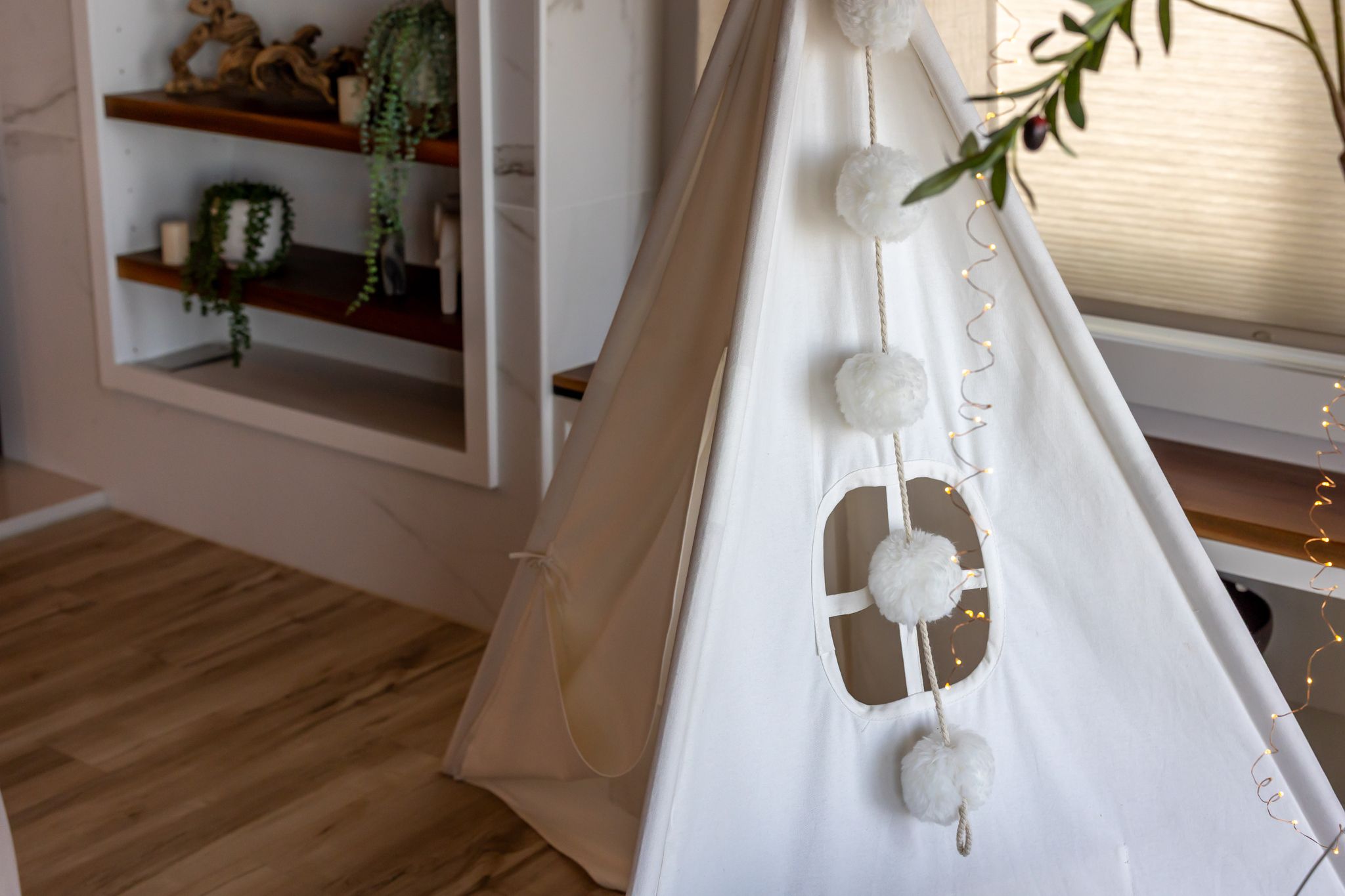A white tent with a rope entrance, decorative pom-poms, and a string of lights.
