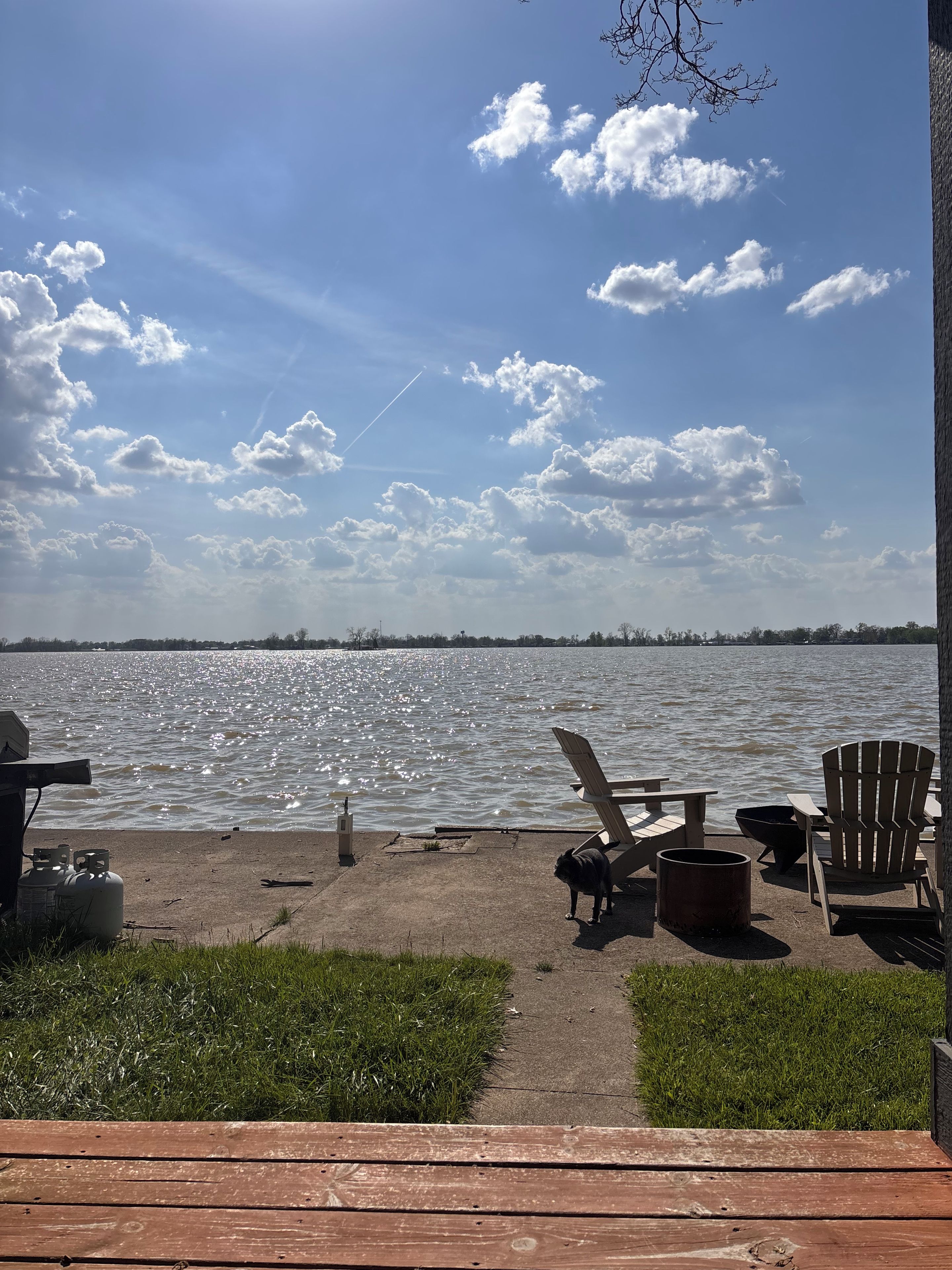 A lakeside deck with outdoor seating, a grill, and propane tanks.
