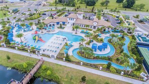 Vista aérea de un complejo turístico con una gran piscina central, varias piscinas más pequeñas y una fuente de agua serpenteante.