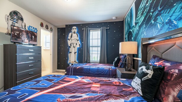 Un dormitorio con ropa de cama temática de Star Wars, un cartel grande de un Stormtrooper y un televisor de Star Wars en el tocador.