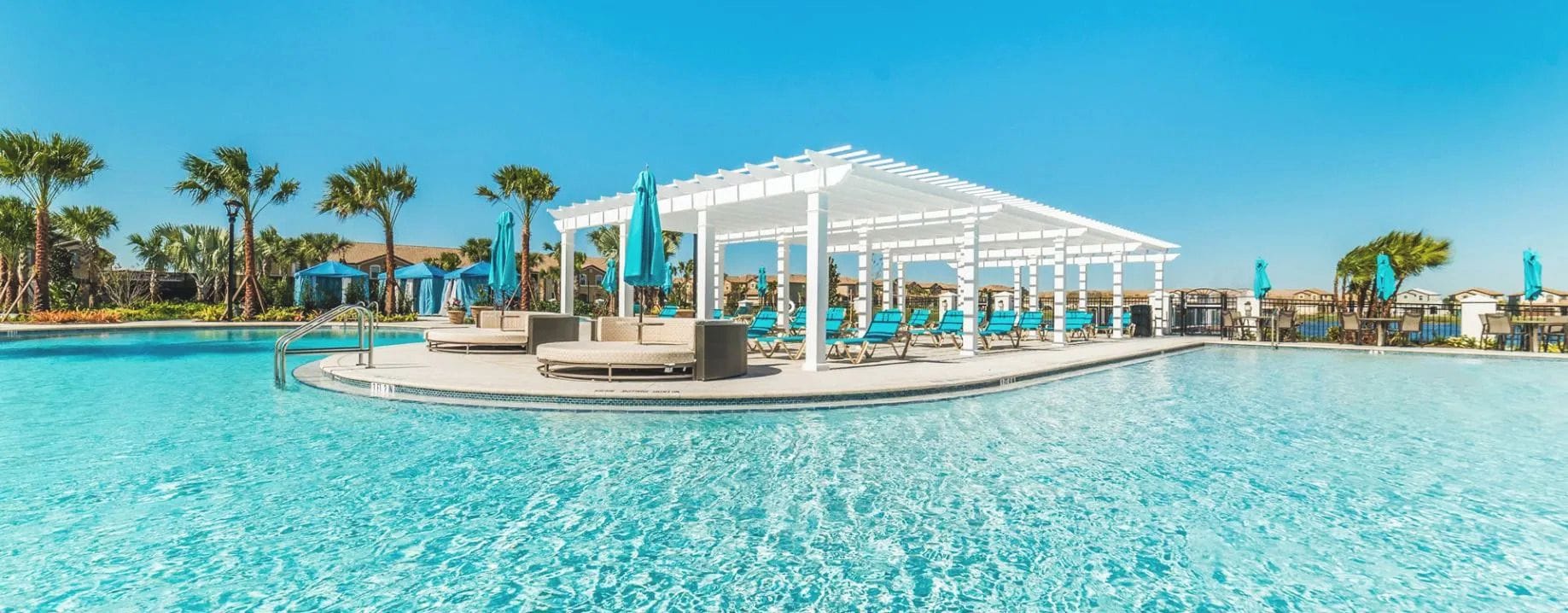 A pool area with a white pergola, lounge chairs, and palm trees.