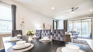 Un comedor moderno con una mesa de madera oscura dispuesta para seis comensales, sillas tapizadas de color gris y un gran ventanal con cortinas.