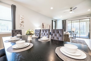 A modern dining room with a dark wooden table set for six, grey upholstered chairs, and a large window with curtains. - Special Offer- 1min walk to Clubhouse, with SPA, Luxury 7BD Home 8900 (Kissimmee)