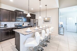 A modern kitchen with dark cabinets, a granite countertop, a central island with bar stools, and pendant lighting. - Special Offer- 1min walk to Clubhouse, with SPA, Luxury 7BD Home 8900 (Kissimmee)