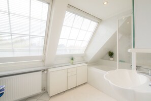 A modern bathroom with a freestanding bathtub, a glass-enclosed shower, and a radiator under a window. - Regina House 11 (Timmendorfer Strand)