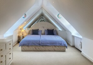 A bedroom with a sloped ceiling, a bed with striped bedding, a bedside lamp, and a dresser. - Regina House 11 (Timmendorfer Strand)