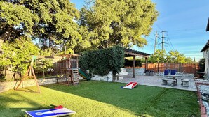 Ein Garten mit Schaukeln, einer Spielanlage, einem Picknicktisch und einem Bocciaspielplatz.