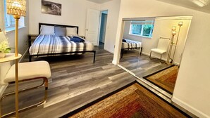 Ein Schlafzimmer mit einem Bett, einem Nachttisch, einem Sessel und einem großen Spiegel.