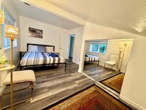 Un dormitorio con cama, mesita de noche, silla y un espejo grande.