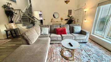 A modern living room with a sectional sofa, a round coffee table, and a staircase.