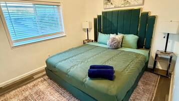 A bedroom with a bed, a window with blinds, a ceiling light, and a wall-mounted artwork.